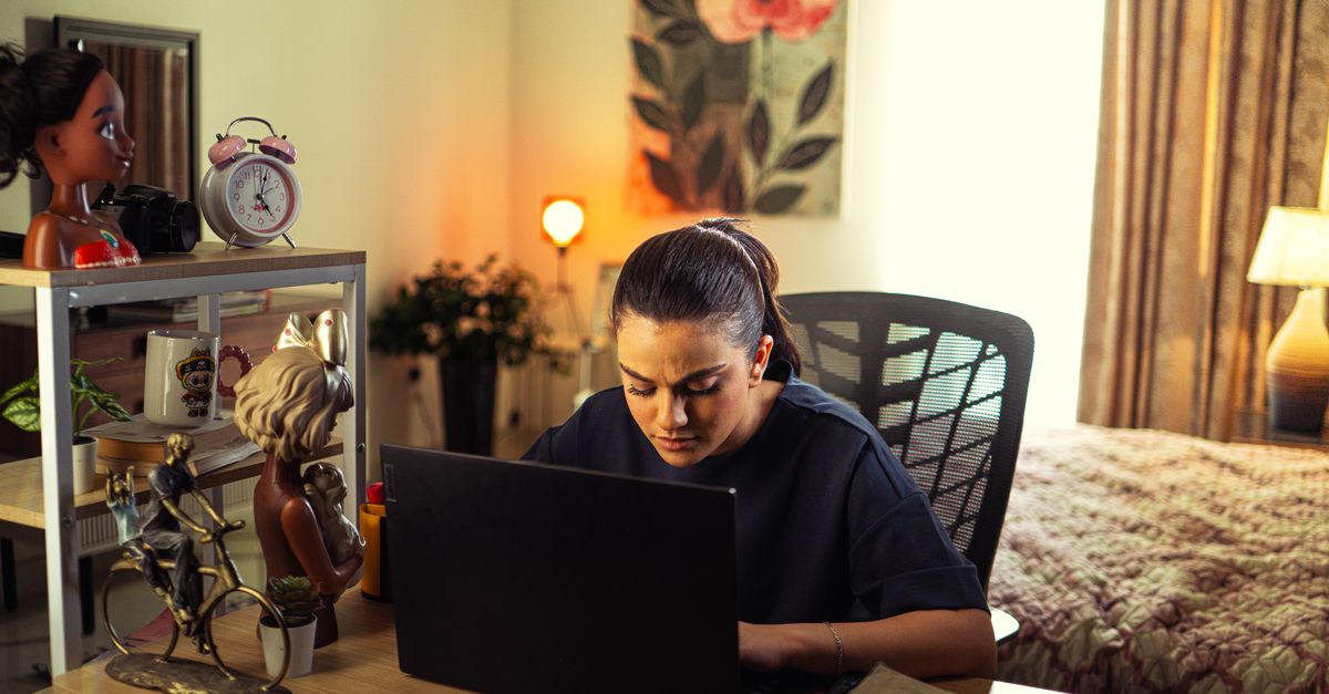 A woman working on a laptop at a home desk in the evening