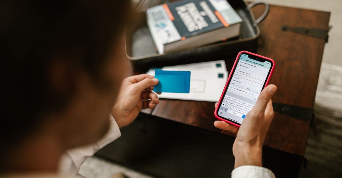 Hands holding a phone and a bank card at a wooden desk while making an online payment