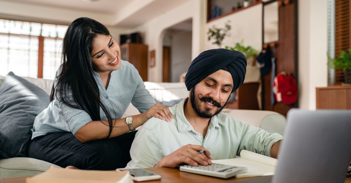 Indian couple at home working out numbers on a calculator beside a laptop