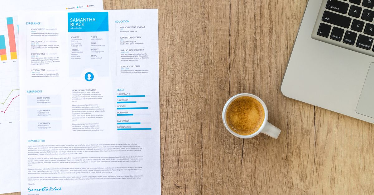 A printed CV on a wooden desk beside a laptop and a cup of coffee