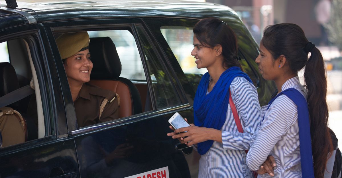 Two women speaking with a police officer beside a patrol vehicle about a cyber complaint.