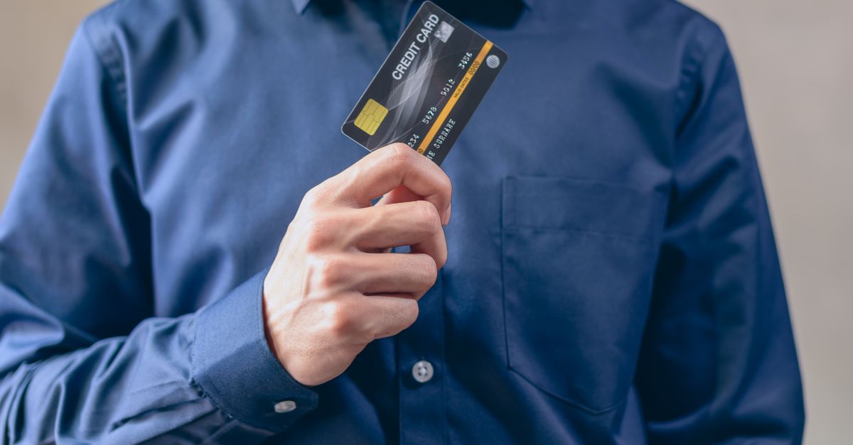 A man in a blue shirt holding out a debit card towards the camera