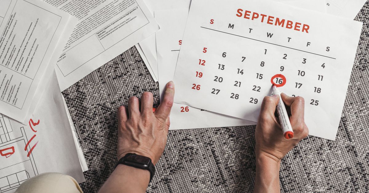 Hands marking a date on a September calendar beside printed documents