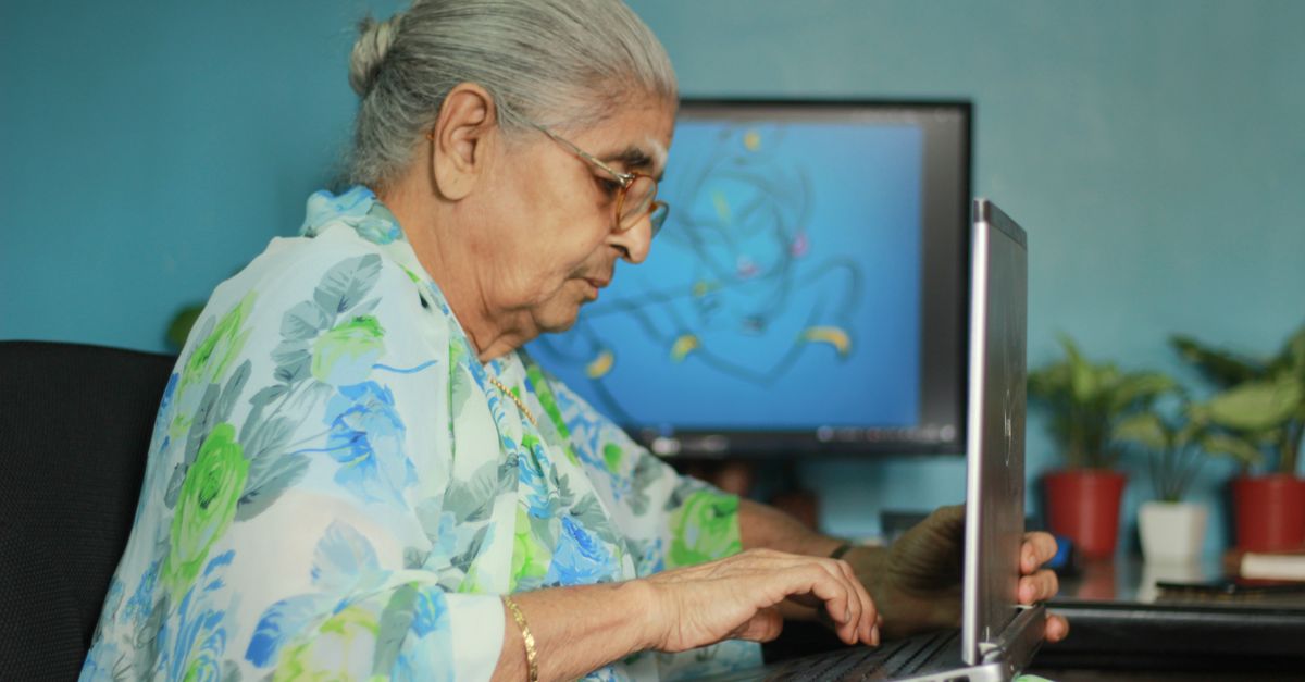An older Indian woman in a printed saree working at a computer at home