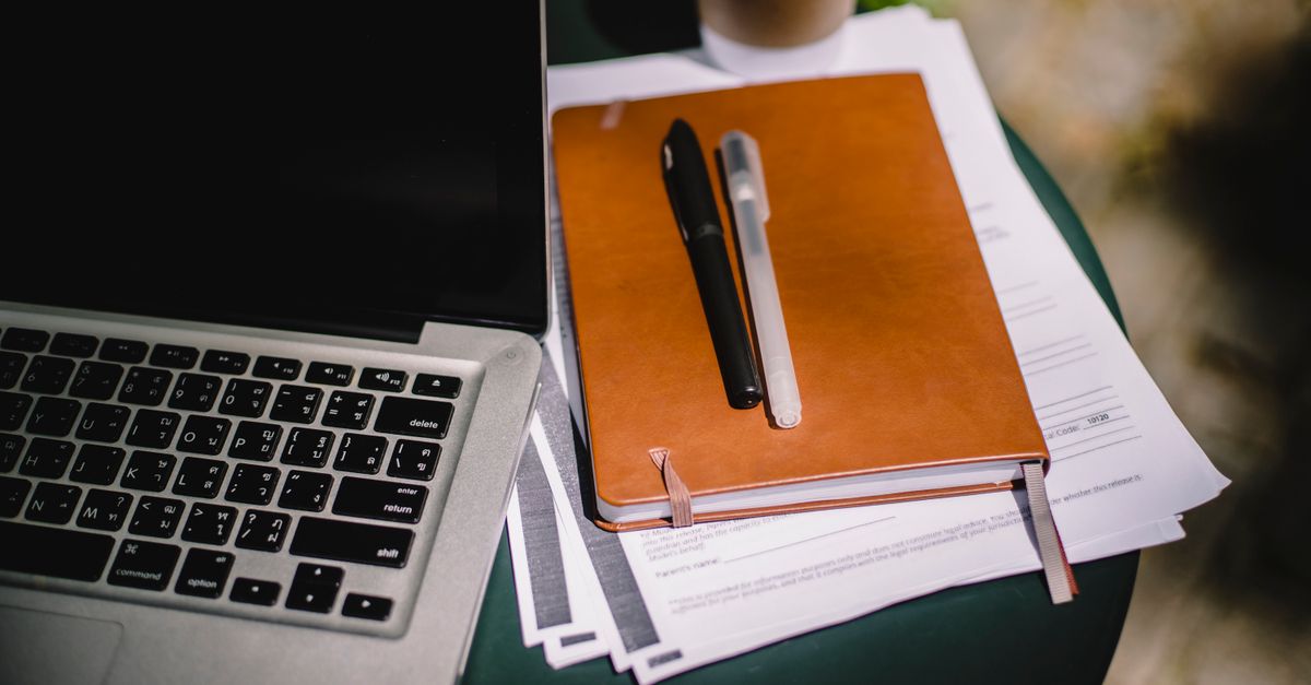 Notebook, pens and papers beside a laptop for checking a work from home job offer